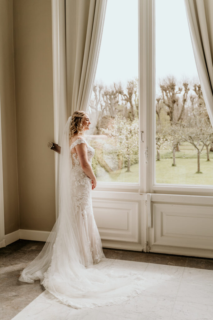 bruid staat bij groot raam naar buiten te kijken
