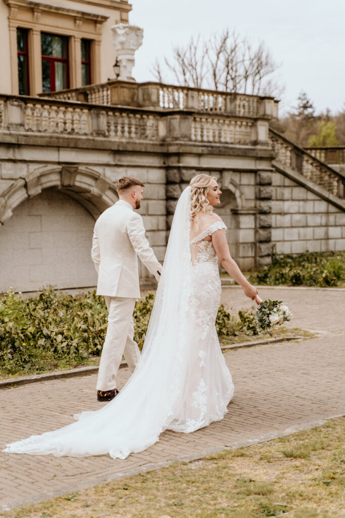 bruidspaar loopt voor een klassiek gebouw hand in hand weg en lacht