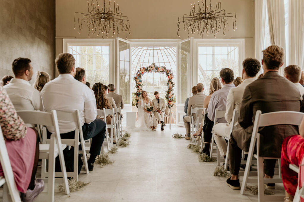 bruidspaar zit op ceremoniebank met gasten om hun heen