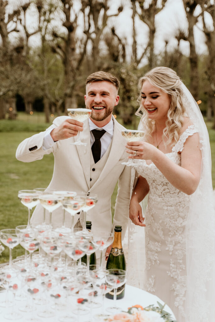 bruidspaar lacht bij champagnetoren met champagne in hun hand